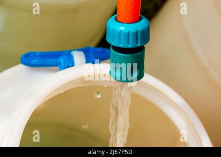 Un jet d'eau provenant d'un tuyau remplit un fût en plastique. Image d'arrière-plan. Le concept de la crise de l'eau potable dans le monde. Banque D'Images