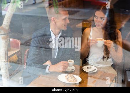 Un couple élégant parle et boit du café à table dans un café. Vue de la rue Banque D'Images