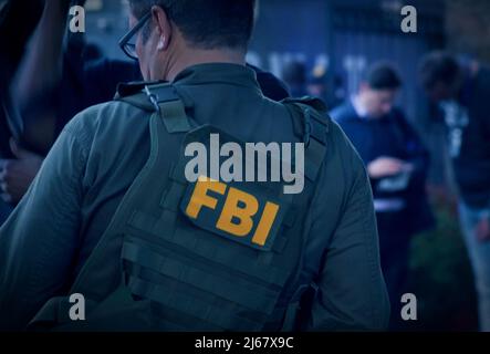 L'agent du FBI masculin caucasien porte des lunettes dans un gilet vert à pare-balles avec le logo du FBI vu de derrière sur l'endroit de l'enquête. Banque D'Images