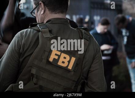 L'agent du FBI masculin caucasien porte des lunettes dans un gilet vert à pare-balles avec le logo du FBI vu de derrière sur l'endroit de l'enquête. Banque D'Images