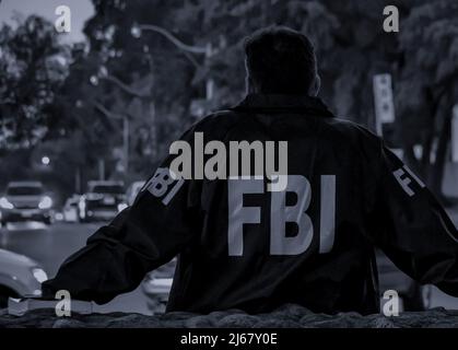 L'agent FBI mâle porte un manteau bleu foncé avec le logo FBI regardant dans la rue avec des voitures au crépuscule vu de derrière. Banque D'Images