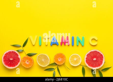 Composition avec du texte VITAMINE C, des moitiés d'agrumes et des feuilles de plantes sur fond jaune Banque D'Images