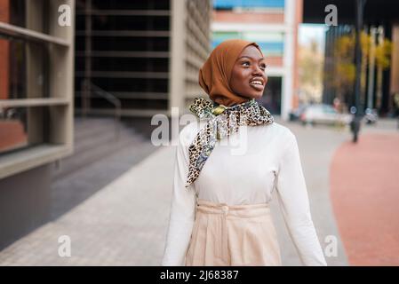 Femme noire musulmane souriante dans un hijab debout près d'un immeuble de bureaux Banque D'Images