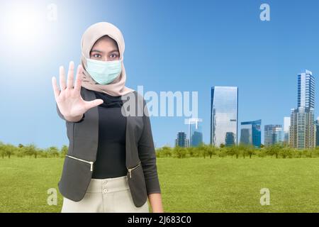 Femme musulmane asiatique portant un foulard et un masque de visage avec un signe d'arrêt sur fond bleu ciel Banque D'Images