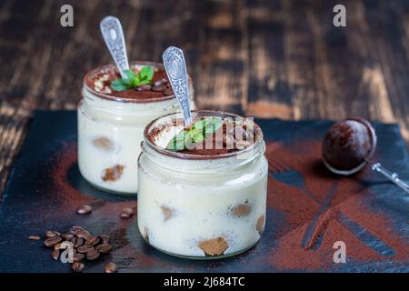 Dessert italien traditionnel tiramisu décoré de poudre de cacao et de menthe verte dans un pot en verre sur la table, gros plan Banque D'Images