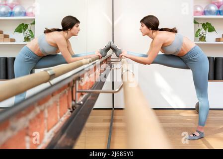 FIT bonne santé jeune femme en train de faire des étirements de jambes sur une barre dans une salle de gym reflétée dans un miroir mural. Concept de fitness Banque D'Images