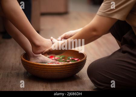 femme pieds trempés dans l'eau avec des pétales dans un bol en bois. Les pieds de femme sont magnifiques au salon de spa sur la procédure de pédicure. Banque D'Images