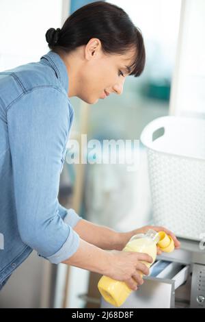 la femme verse le détergent liquide à laver dans la machine Banque D'Images
