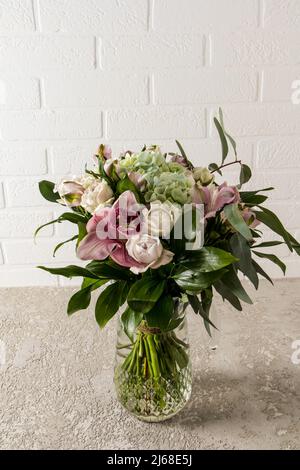 un bouquet chic de roses et d'hortensias dans un vase en verre se dresse sur une table contre un mur de briques blanches. Un cadeau parfait pour vos proches Banque D'Images