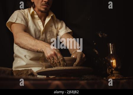 homme dans atelier de poterie fait plaque d'argile, une atmosphère authentique, lampe jaune, style de vie, atmosphère magique. Concept avec vos propres mains, maison fr Banque D'Images