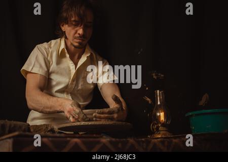 homme dans atelier de poterie fait plaque d'argile, une atmosphère authentique, lampe jaune, style de vie, atmosphère magique. Concept avec vos propres mains, Home Entertainment. Fond noir Banque D'Images