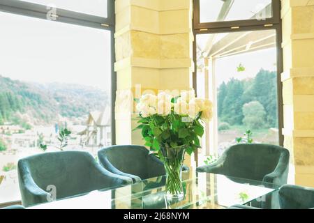 Roses blanches dans un vase sur une table en verre et des chaises vertes. Fleurs sur le bureau dans la salle de réunion et le fauteuil Banque D'Images