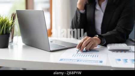 Une femme d'affaires ou de garde-livres pointe le chiffre d'affaires avec rapport graphique et utilise un ordinateur portable pour l'analyse des données Banque D'Images