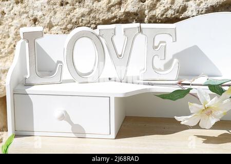 Mot amour avec des lettres en bois blanc sur un mobilier blanc décorant un jardin un jour ensoleillé. Banque D'Images