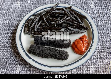 Une assiette de frites et de doigts de poisson très brûlés, noirs. Banque D'Images