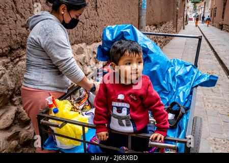 Un enfant assis dans Un chariot mobile dans la ville de Pisac, la Vallée Sacrée, province de Calca, Pérou. Banque D'Images