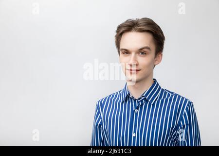 Portrait d'un jeune homme confiant et joyeux portant une chemise bleue-blanche à rayures boutons regardant l'appareil photo avec un sourcil relevé. Studio tourné sur la bande grise Banque D'Images