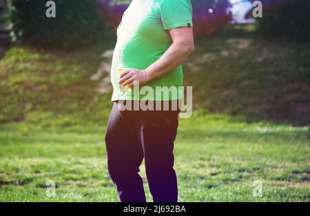 Oerweight homme portant une chemise verte, buvant une bouteille de bière dans un parc . Banque D'Images