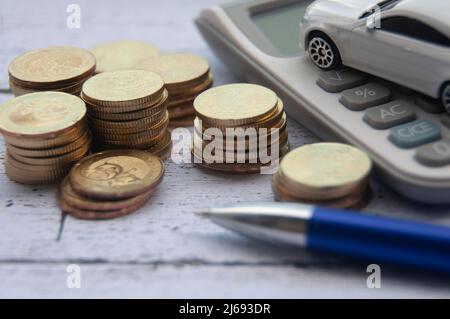 Pièces d'or, calculatrice, jouet de voiture blanc et stylo sur fond de bois. Accent sélectif sur les pièces. Concept de finance et d'espace de copie Banque D'Images