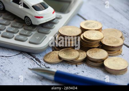 Pièces d'or, calculatrice, jouet de voiture blanc et stylo sur fond de bois. Accent sélectif sur les pièces. Concept de finance et d'espace de copie Banque D'Images