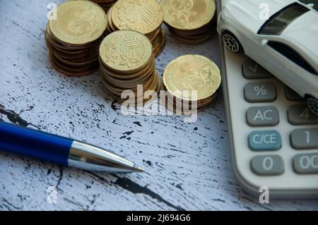 Pièces d'or, calculatrice, jouet de voiture blanc et stylo sur fond de bois. Accent sélectif sur les pièces. Concept de finance et d'espace de copie Banque D'Images