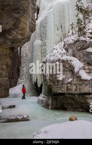 Un homme portant un manteau rouge se tenait dans le canyon Maligne pendant les conditions hivernales, parc national Jasper, site du patrimoine mondial de l'UNESCO, Alberta, Canada Banque D'Images