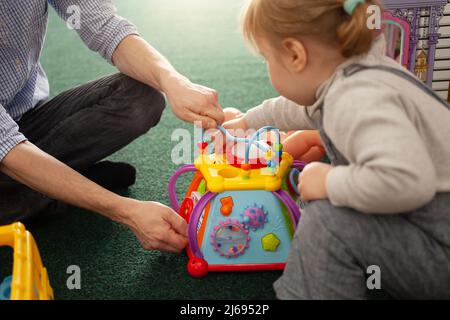 Une petite fille de deux ans joue avec des jouets dans la salle de jeux. Centre de développement, jardin d'enfants et fille jouent sur le tapis avec un jouet multicolore Banque D'Images