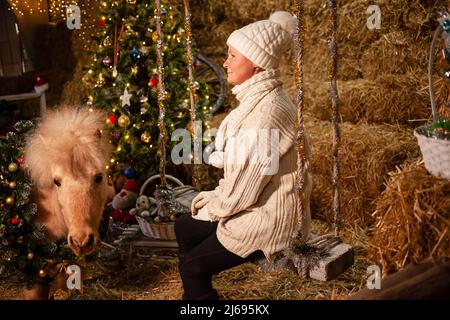 Décorations de Noël sur les écuries. Un magnifique poney avec une couronne autour de son cou. Arbre de Noël avec ballons, zone photo pour le nouvel an. Femme senior Banque D'Images