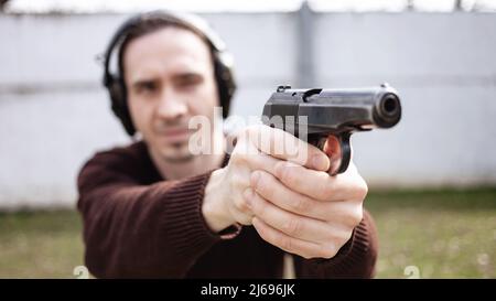 Un jeune homme cherche un fusil. Un homme portant un casque de protection. Gamme de tir de pneu extérieur. Hobby. Arme à feu contre le mur blanc Banque D'Images