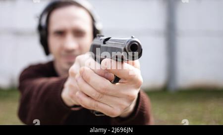 Un jeune homme cherche un fusil. Un homme portant un casque de protection. Gamme de tir de pneu extérieur. Hobby. Arme à feu contre le mur blanc Banque D'Images