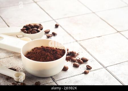 Fond de café. Cuillères à mesurer avec du café moulu et des grains sur un fond de table vieux carrelage fissuré. Ingrédients pour faire du café. Vue de dessus avec sp Banque D'Images