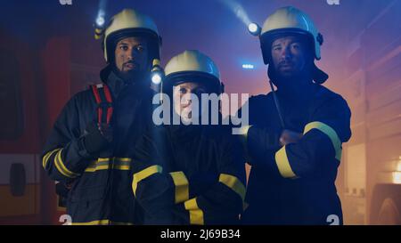 Pompiers hommes et femmes à l'action avec un camion d'incendie en arrière-plan la nuit Banque D'Images