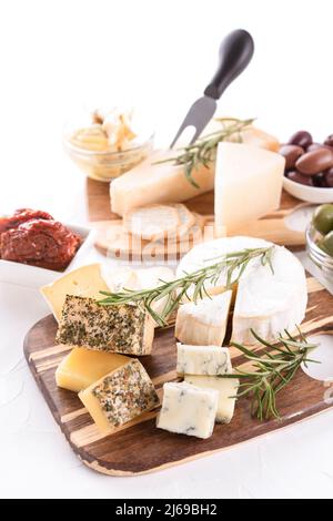 Plateau de fromages en bois avec sélection de fromages servis avec des olives et des tomates séchées sur table blanche. Assiette de fromages avec des fromages artisanaux pour un Banque D'Images