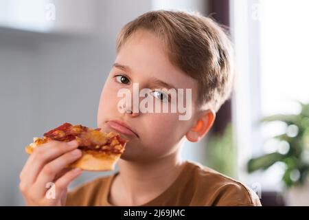 Un jeune garçon triste qui apprécie de manger une délicieuse pizza à la maison. Banque D'Images