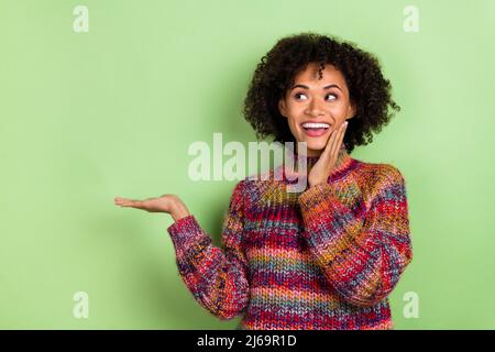 Portrait de fille stupéfait joue de main regarder intéressé paume tenir espace vide isolé sur fond vert couleur Banque D'Images