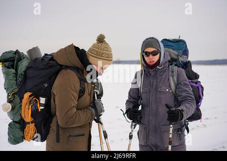 Deux gars marchent dans la neige au cours d'une expédition d'hiver. Ils portent de grands sacs à dos et des vestes chaudes. Ils tiennent des bâtons de randonnée dans leurs mains. Banque D'Images