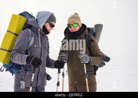 Deux gars marchent dans la neige au cours d'une expédition d'hiver. Ils portent de grands sacs à dos et des vestes chaudes. Ils tiennent des bâtons de randonnée dans leurs mains. Banque D'Images