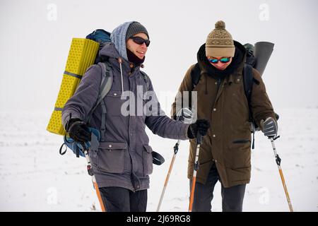 Deux gars marchent dans la neige au cours d'une expédition d'hiver. Ils portent de grands sacs à dos et des vestes chaudes. Ils tiennent des bâtons de randonnée dans leurs mains. Banque D'Images