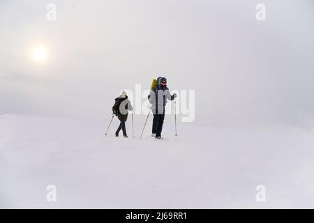 Les gars parlent pendant l'expédition d'hiver. Ils portent des vestes chaudes, des chapeaux et de grands sacs à dos. Ils se tiennent dans la neige et tiennent des bâtons de randonnée Banque D'Images