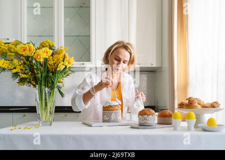 Une femme dans la cuisine décore les pâtisseries de pâques. Banque D'Images