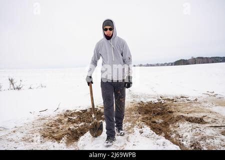 Le gars dans la boue après avoir creusé un trou dans la neige. Saleté sur les pantalons et les vêtements Banque D'Images