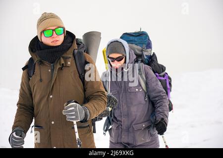 Deux gars marchent dans la neige au cours d'une expédition d'hiver. Ils portent de grands sacs à dos et des vestes chaudes. Ils tiennent des bâtons de randonnée dans leurs mains. Banque D'Images