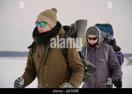 Deux gars marchent dans la neige au cours d'une expédition d'hiver. Ils portent de grands sacs à dos et des vestes chaudes. Ils tiennent des bâtons de randonnée dans leurs mains. Banque D'Images