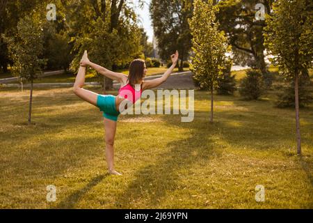Femme attirante pratiquant le yoga. Belle jeune brunette exécute des étirements dans l'exercice Natarajasana, pose du Seigneur de la danse, formation dans la nature Banque D'Images
