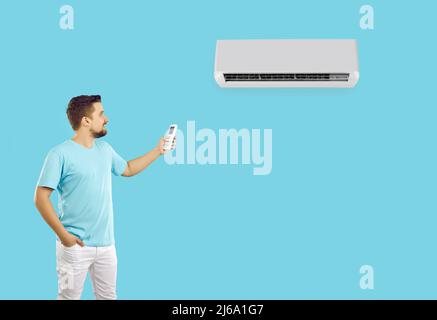 Un jeune homme heureux utilisant la télécommande allume ou règle la climatisation sur fond bleu clair. Banque D'Images
