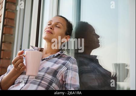 Belle femme d'âge moyen se détend dans le balcon de sa maison de campagne et apprécie son café du matin Banque D'Images