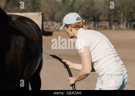 Femme caucasienne mature, 40 ans, se lavant de cheval sale avec le tuyau à l'extérieur. Banque D'Images