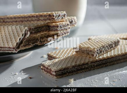 biscuits de cachets sur une assiette noire et sur une table blanche, avec un verre de lait froid sur le côté éclairé par la lumière du soleil provenant d'une fenêtre Banque D'Images