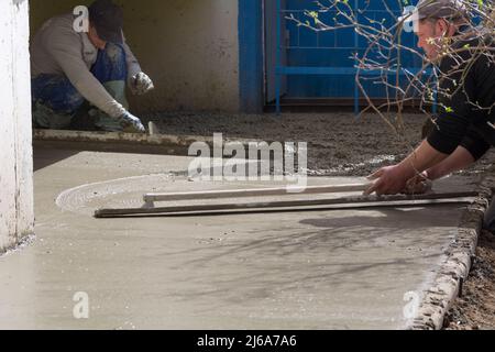 Tiraspol, Moldova - 1, avril 2022 : les travailleurs construisent une zone aveugle de la fondation de la maison. Le travailleur de la construction aligne la table en béton. Constructio Banque D'Images