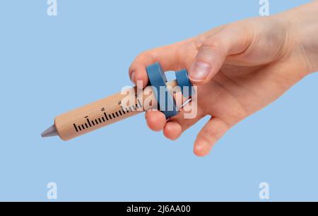 Femme tenant main modèle de seringue en bois pour la médecine, vaccin, injection de drogues sur fond bleu. Soins de santé, concept de traitement médical. Photo de haute qualité Banque D'Images